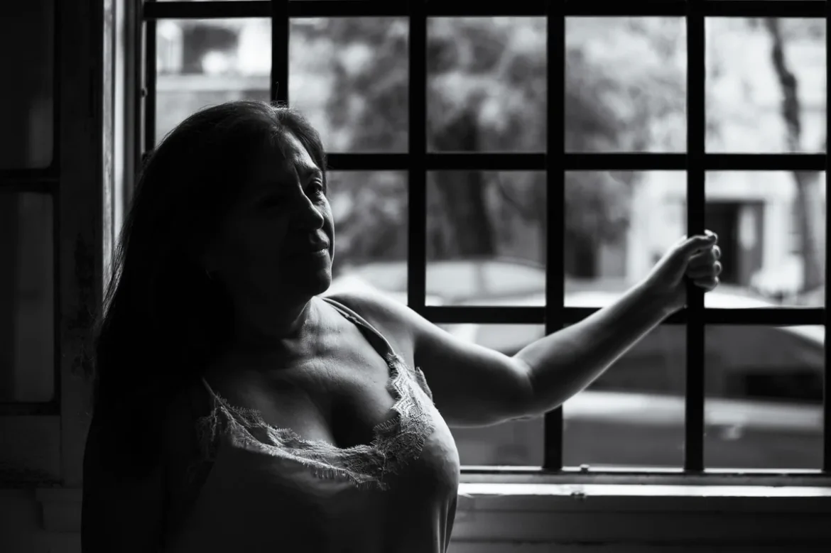 Femme en vêtements légers près d'une fenêtre ouverte, cherchant du soulagement et de la fraîcheur