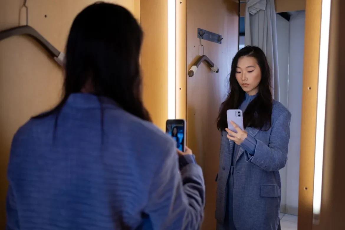 Femme observant sa silhouette dans un miroir, vêtue d'un blazer structuré et d'un pantalon taille haute.