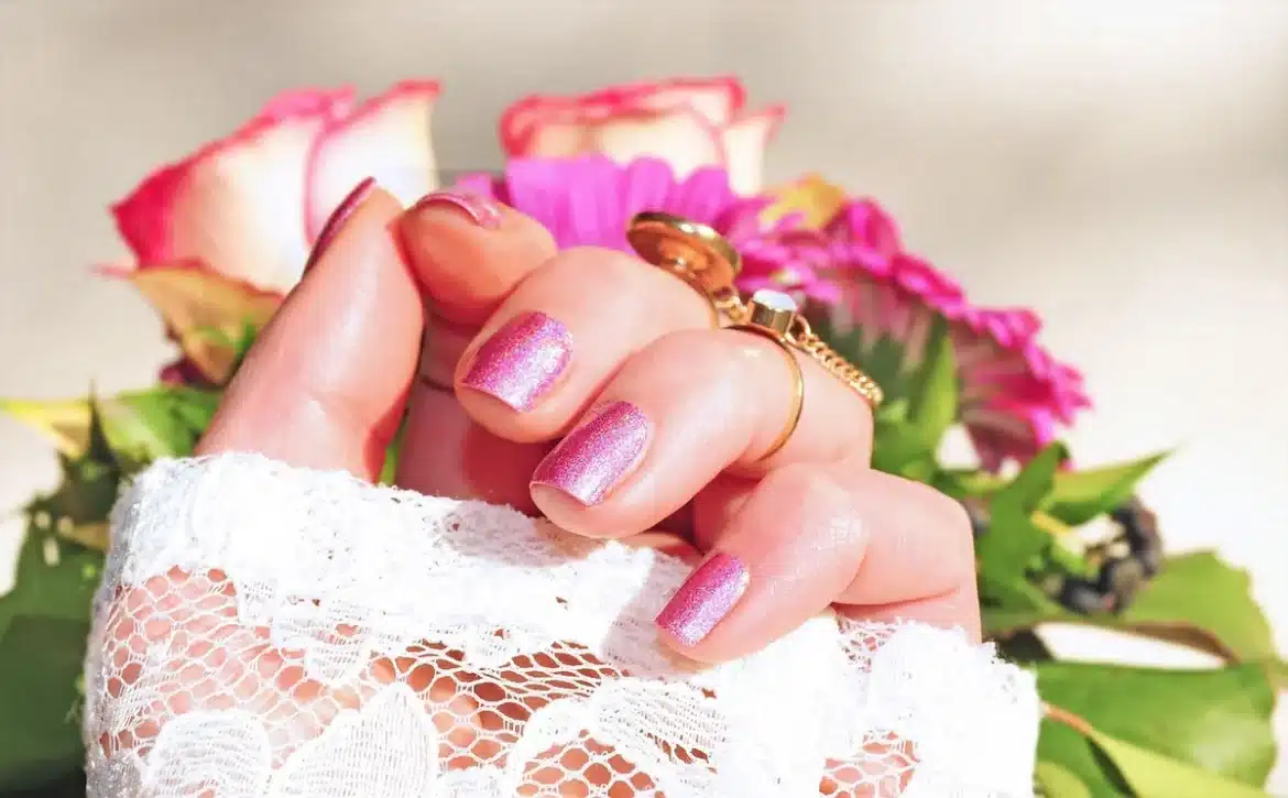 Gros plan de mains manucurées avec vernis à ongles de couleurs hivernales profondes sur fond texturé chaleureux