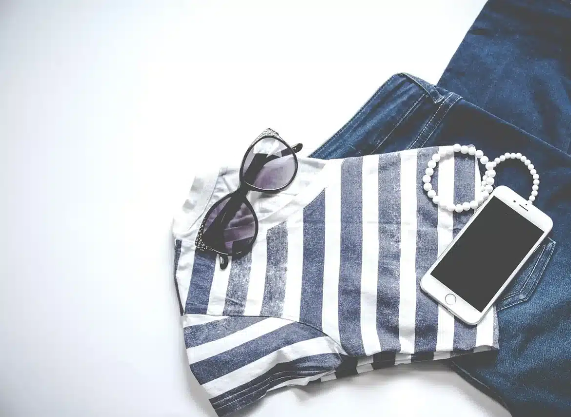 Coin dressing clair avec pull plié, blazer suspendu et sneakers près d'une fenêtre en journée
